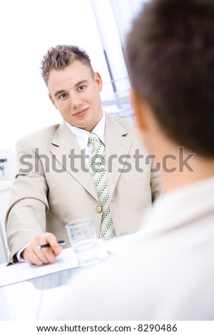 Two businessmen sitting by desk, discussing, over the shoulder view.