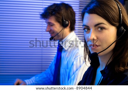 Customer service team working in headsets, late night at office. Focus placed on woman in front.