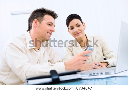 Businesspeople looking at cellphone screen, smiling.