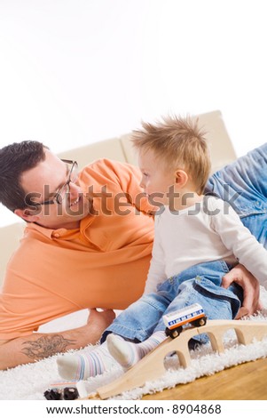 Father and two year old child playing together with wooden toy train. Sitting on floor at home, smiling.