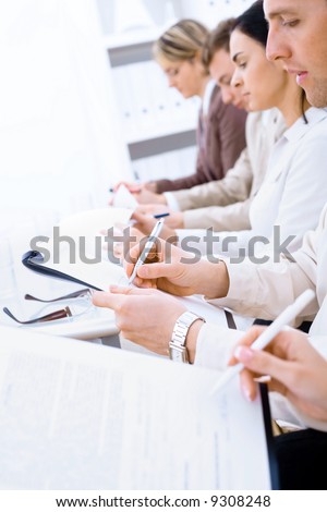 Business people sitting in a row and writing notes.  Selective focus placed on writing hand. Browse my portfolio for horizontal version.