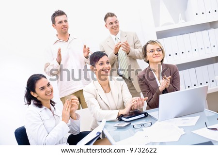 Group of five happy business people smiling and clapping, looking at same direction.