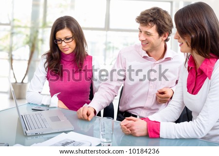 Happy young business people having meeting at office, looking at laptop computer, smiling.