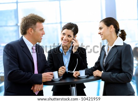 Young and happy business people standing around coffee table, drinking coffee and talking, smiling, indoor.