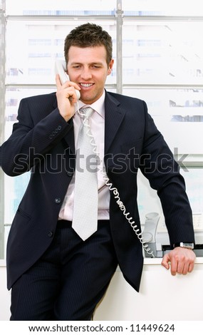 Mature happy businessman calling on landline phone at office, smiling.