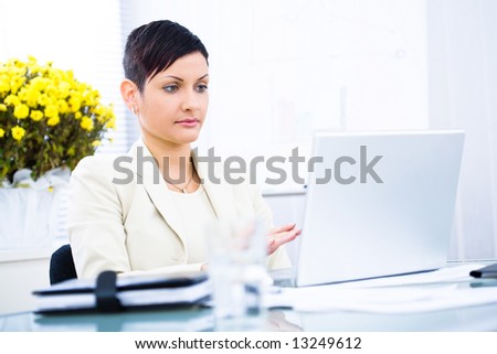 Businesswoman working on laptop computer in brightly lit office, serious.