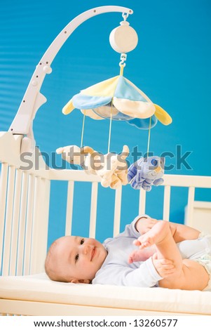4 months old happy baby boy lying on crib playing with his cute little feet, smiling. Toys are officially property released.