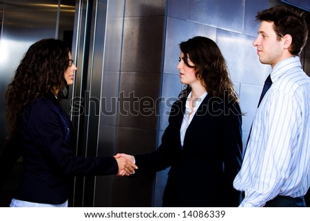 Smiling business people shaking hands at office lobby in front of elevator.