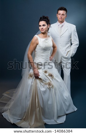 Happy bride and groom posing together in studio, wearing wedding dress, smiling.