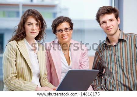 Happy young business people having meeting at office, working in team together on laptop computer, smiling.