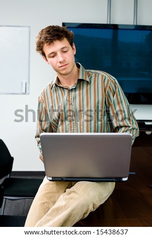 Young office worker sitting on meeting table at office and working on laptop computer.