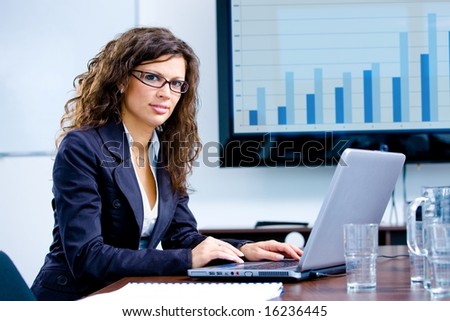 Young happy businesswoman working on laptop computer in meeting room at office, looking at camera smiling.