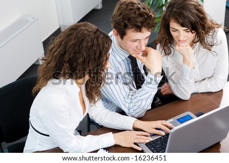 Happy young business people sitting by table at office, working together on laptop computer, smiling. High-angle view.