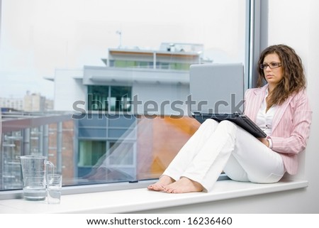 Young creative businesswoman sitting at office window and working on laptop computer.
