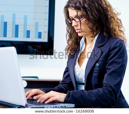 Young businesswoman working on laptop computer in meeting room at office with TV-screen and graph in background.