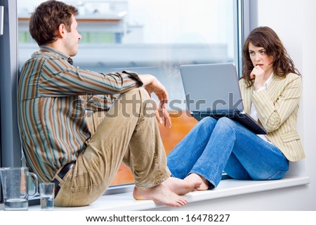 Businessman and businesswoman having creative meeting,  sitting in office window working on laptop computer and talking.