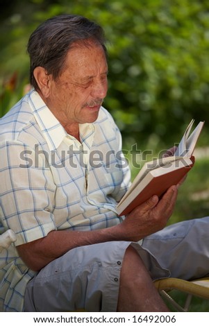 Healthy looking aged man is his late 70s sitting in garden at home and reading book.