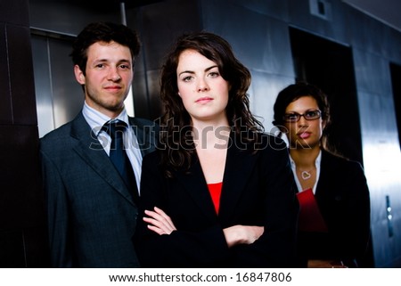 Portrait of successful happy business team posing at office lobby in front of elevator. Dark background.