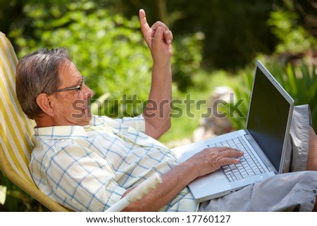 Healthy senior man is his elderly 70s sitting outdoor in garden at home and using laptop computer to browse internet.