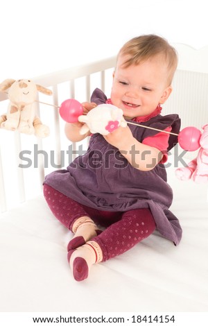 Cute baby girl (1 year old) sitting on crib, holding soft toys. Isolated on white, smiling. Toys are offically property released.