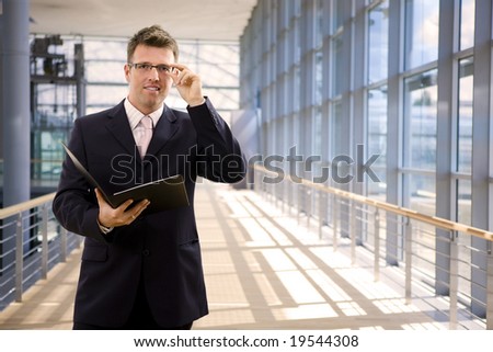 Happy single businessman holding folder, smiling at office lobby.