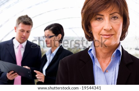 Senior businesswoman with working business team in background.