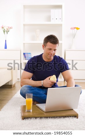 Mid-adult man working on laptop computer at home, sitting on floor.