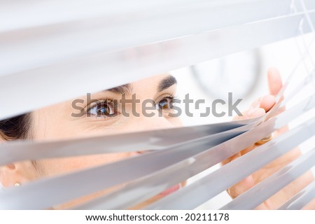 Woman peeping though window blinds, smiling.