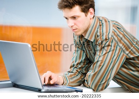 Casual looking businessman working on laptop computer in front of office window.