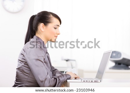 Businesswoman working hard on her laptop computer in brightly lit office.
