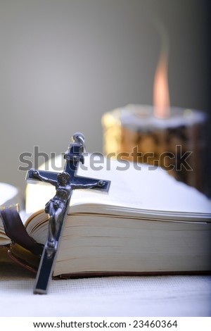Old Cross and the Holy Bible laying on the table in fornt of a lighting candle.