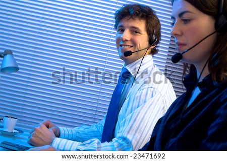 Customer service team working in headsets, late night at office. Focus placed on smiling man in back.