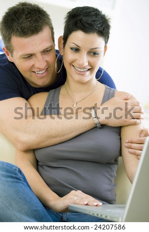 Happy young couple browsing internet on laptop computer at home, smiling.