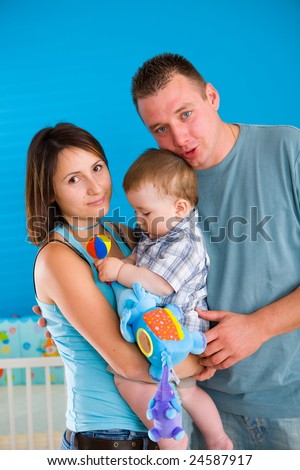 Portrait of happy family at home. Baby boy ( 1 year old ) and young parents father and mother posing together at children\'s room, smiling.