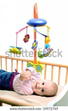 Happy baby playing with bed side toy, smiling, isolated on white background.