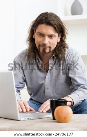Casual man using laptop computer at home, smiling and looking at screen.