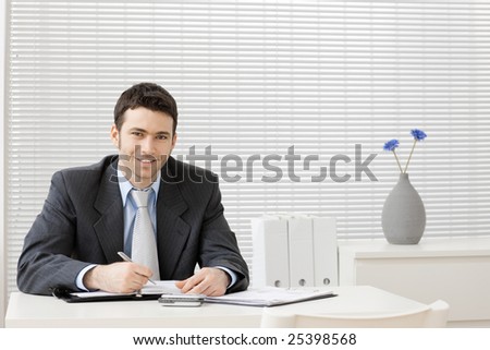 Happy young businessman working at desk at office, smiling.