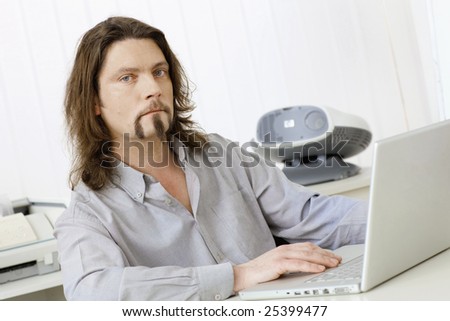 Portrait of casual businessman working at desk using laptop computer, looking at screen.