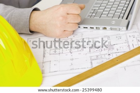 Floor plan on architect\'s desk along with laptop computer, yellow hardhat and ruler.