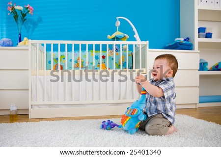 Happy baby boy ( 1 year old ) sitting on floor at home and playing with soft toys at children\'s room, smiling.