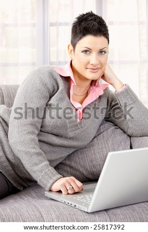 Young woman sitting on couch working on laptop computer at home.