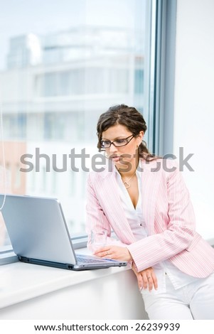 Young attractive businesswoman browsing internet on laptop computer in fron front of office window.
