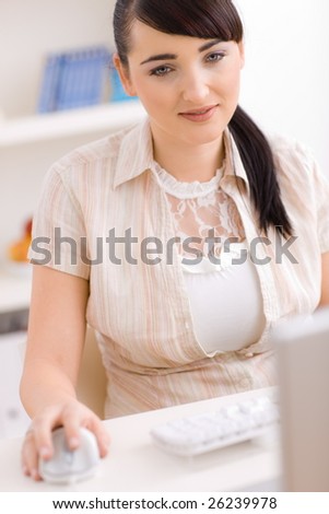 Young woman working using laptop computer and mouse, smiling and looking at screen.