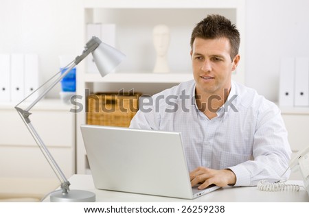 Casual young businessman working at home on laptop compuer, looking at screen.
