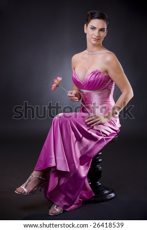 Beautiful young woman sitting on a chair wearing purple evening dress holding a flower.