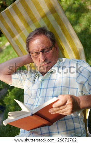 Healthy looking senior man is his late 70s sitting in garden at home and reading book, outdoor.