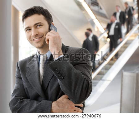 Young smiling businessman calling on phone at office.