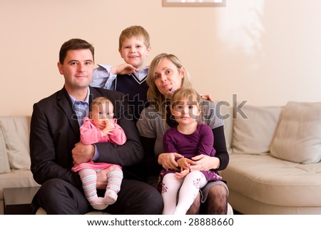 Portrait of happy family sitting on couch at home, smiling: father, mother, son, younger sister and a baby girl.