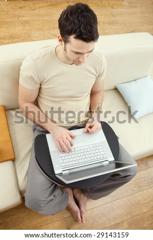 Young man sitting on sofa at home using laptop computer, overhead view.