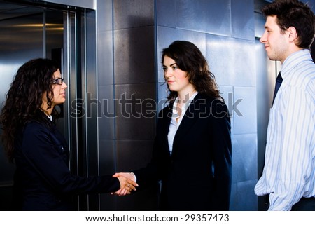 Smiling business people shaking hands at office lobby in front of elevator.